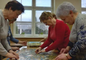 Seniorzy z Klubu "Senior+" układają puzzle.
